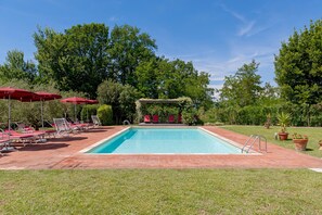 Une piscine rectangulaire avec une terrasse carrelée, entourée de parasols rouges et de chaises longues.