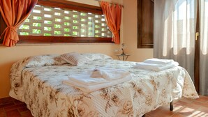Ein Schlafzimmer mit Bett, Vorhängen, einem Fenster mit Gitterwerk und einem kleinen Tisch mit Lampe.