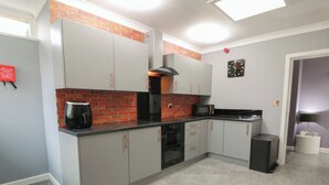 A kitchen with grey cabinets, a brick backsplash, a microwave, a coffee maker, and a trash bin. - Shotts Cottage (Stirling)