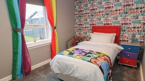 A bedroom with a bed, a nightstand, a dresser, a window with curtains, and a wall with graffiti art. - Shotts Cottage (Stirling)