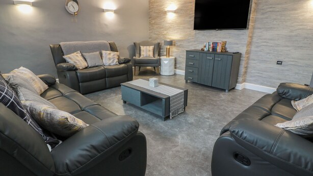 A modern living room with a sofa set, a coffee table, a cabinet, and a flat-screen TV mounted on the wall. - Shotts Cottage (Stirling)