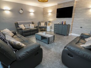 A modern living room with a sofa set, a coffee table, a cabinet, and a flat-screen TV mounted on the wall. - Shotts Cottage (Stirling)