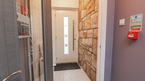 A hallway with a stone wall, a door with a frosted glass panel, and a red emergency pull station on the wall. - Shotts Cottage (Stirling)