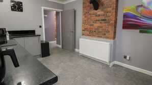 A kitchen with a microwave, a black countertop, a door leading to another room, a white radiator, and a brick wall with a mounted deer head. - Shotts Cottage (Stirling)