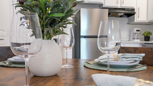 Una mesa de comedor dispuesta con vasos transparentes, un florero texturizado y servilletas dobladas con cuidado.