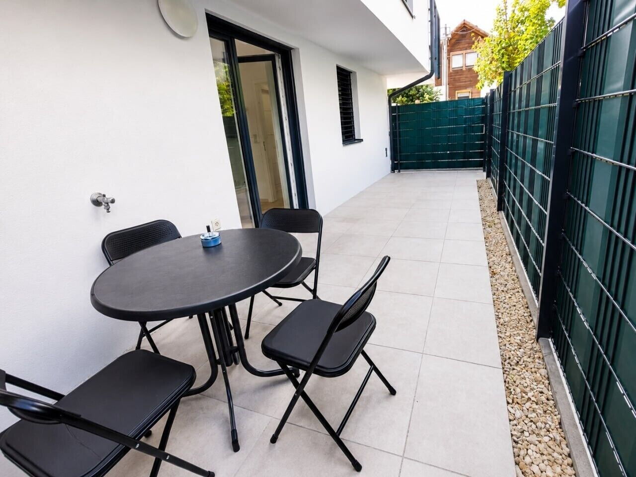 An outdoor patio with a round table and four chairs, a door, and a green fence.