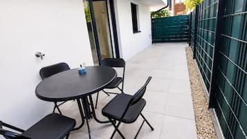 An outdoor patio with a round table and four chairs, a door, and a green fence.