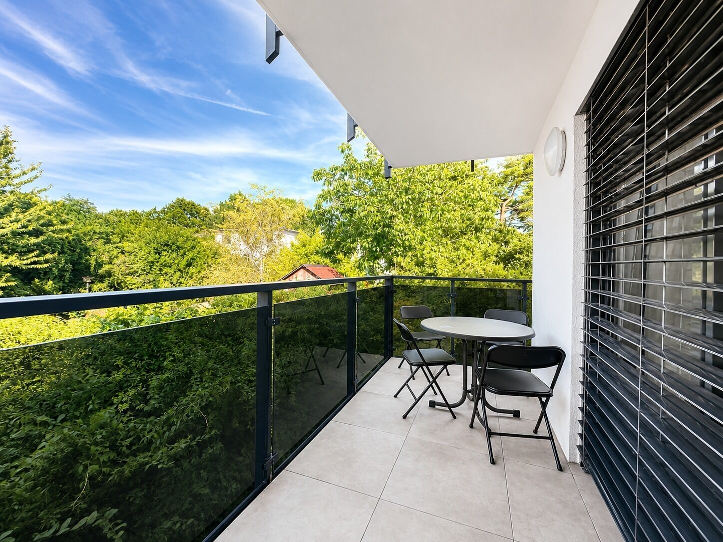 A balcony with a table and chairs, a view of greenery, and a building in the background.
