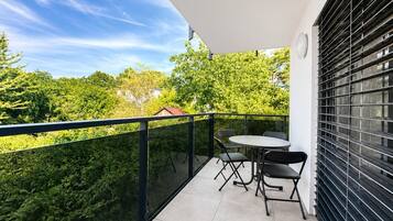 A balcony with a table and chairs, a view of greenery, and a building in the background.