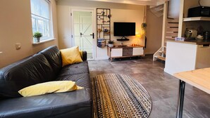Una sala de estar moderna con un sofá de cuero, un televisor de pantalla plana, una mesa de centro y una escalera que lleva a un nivel superior.