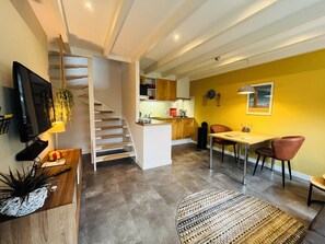 Une cuisine moderne avec un escalier, un coin repas avec des chaises et un téléviseur fixé au mur.