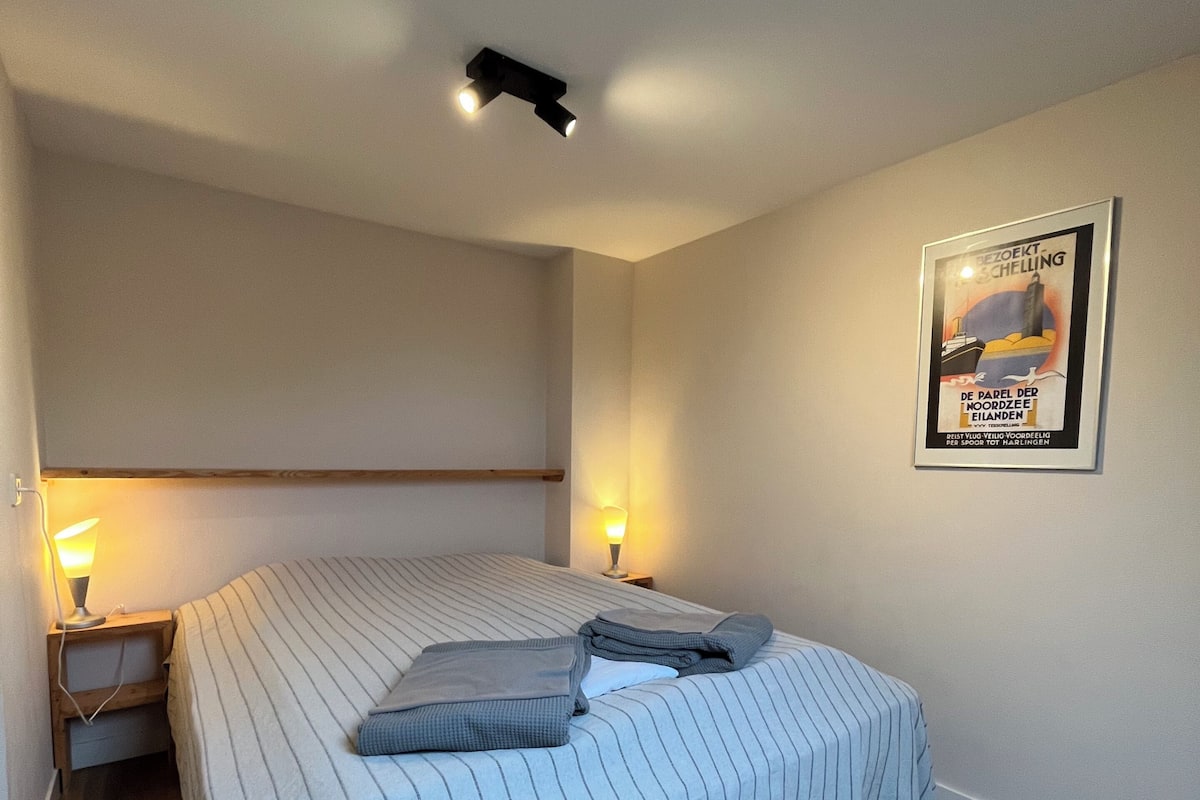 A bedroom with a bed, bedside lamps, a framed picture on the wall, and a ceiling light.