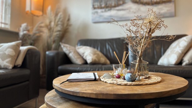 Una sala de estar acogedora con una mesa de centro redonda de madera, un libro, caracolas decorativas y plantas secas.