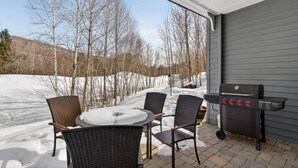 En overdækket terrasse med grill, fire stole og et bord.