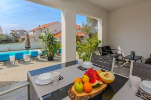 Ein Balkon mit Frühstückstisch, einem Pool und Blick auf Häuser.