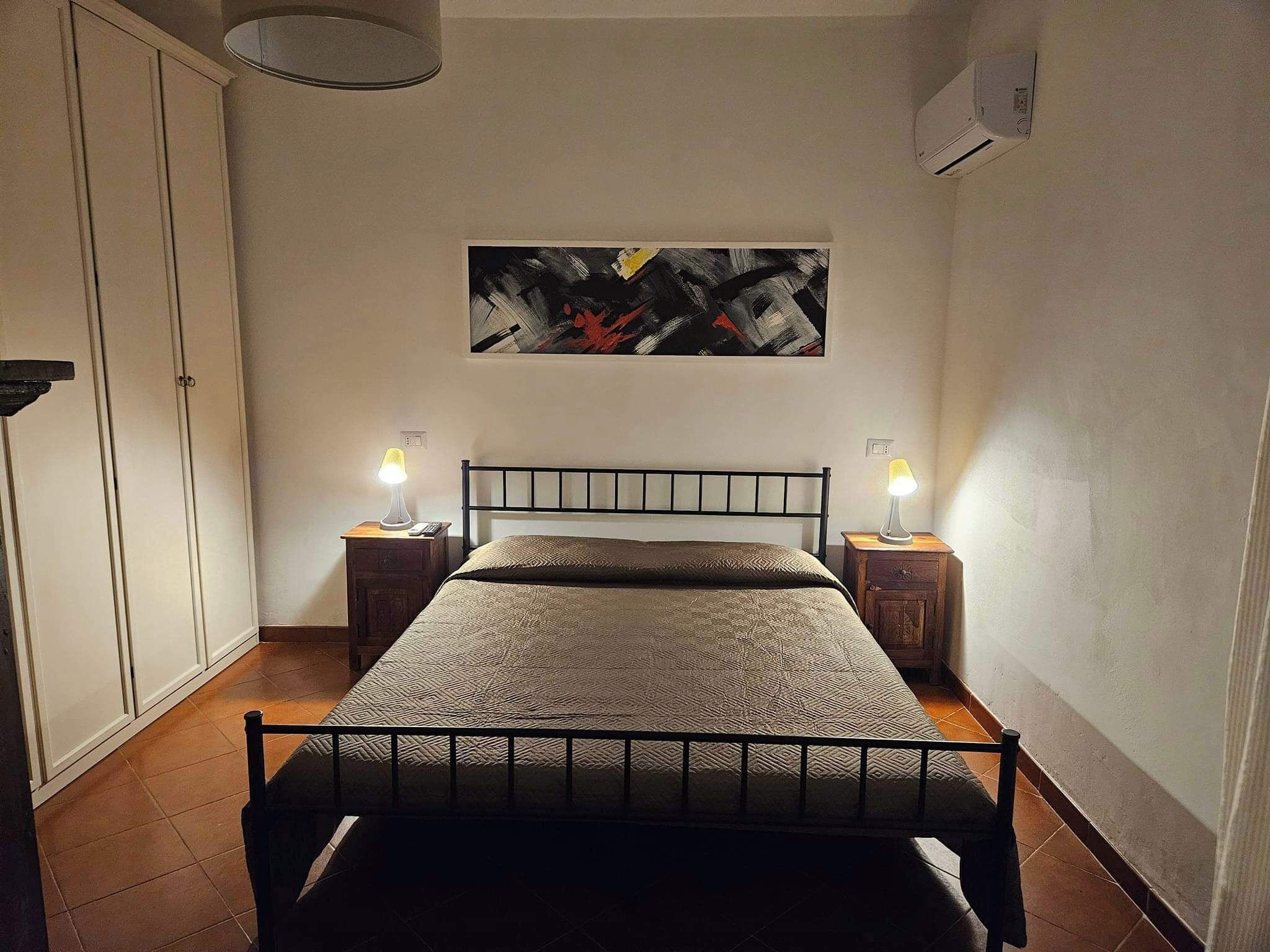 A bedroom with a bed, two bedside tables with lamps, a painting on the wall, and a wardrobe.