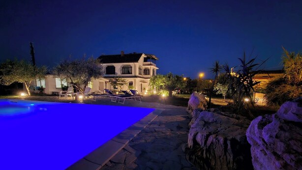 Vista nocturna de una casa con piscina, camino de piedra y zona de estar al aire libre.