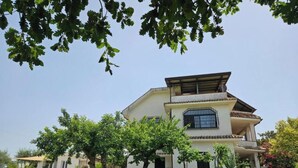 Una casa de dos pisos con un balcón, rodeada de un césped cuidado y árboles.