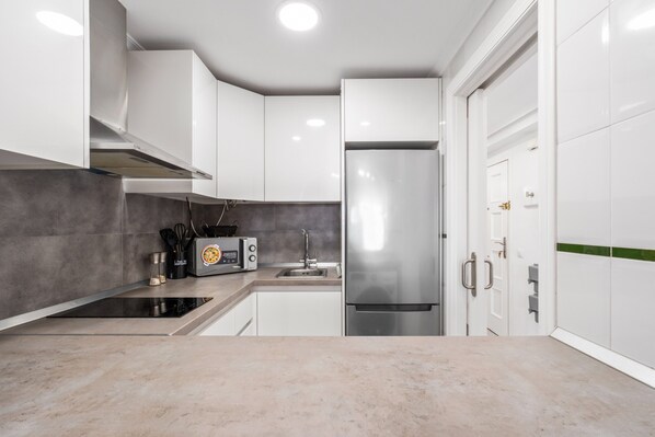 Eine moderne Küche mit weißen Schränken, einem Edelstahl-Kühlschrank, einem eingebauten Backofen und einem Spülbecken.