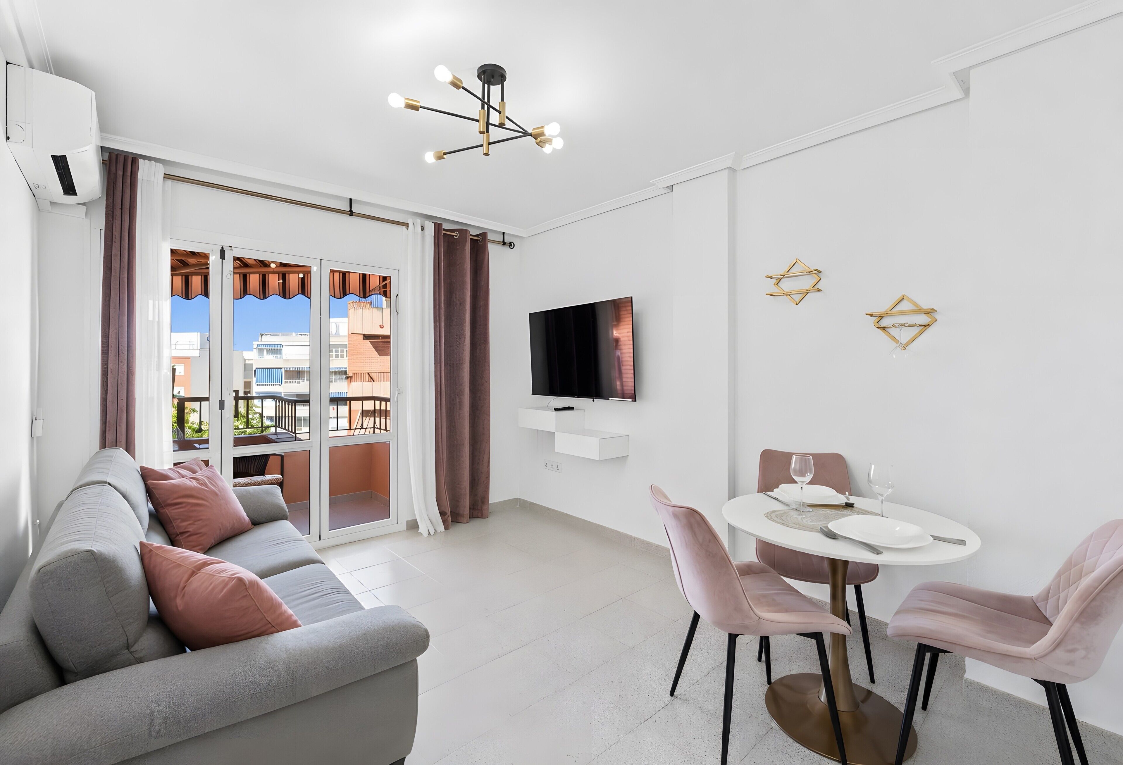 Una sala moderna con sofá, una mesa de comedor con sillas, televisor de pantalla plana montado en la pared y un balcón con cortinas.