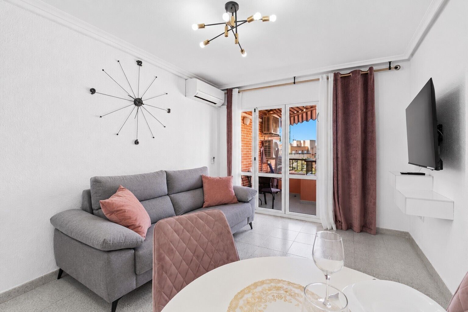 Una sala de estar moderna con un sofá gris, un aire acondicionado instalado en la pared, una lámpara de techo y un ventanal corredero que da a un espacio exterior.
