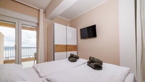 Ein Hotelzimmer mit Balkon, einem Wandfernseher und zwei Betten mit Handtüchern.