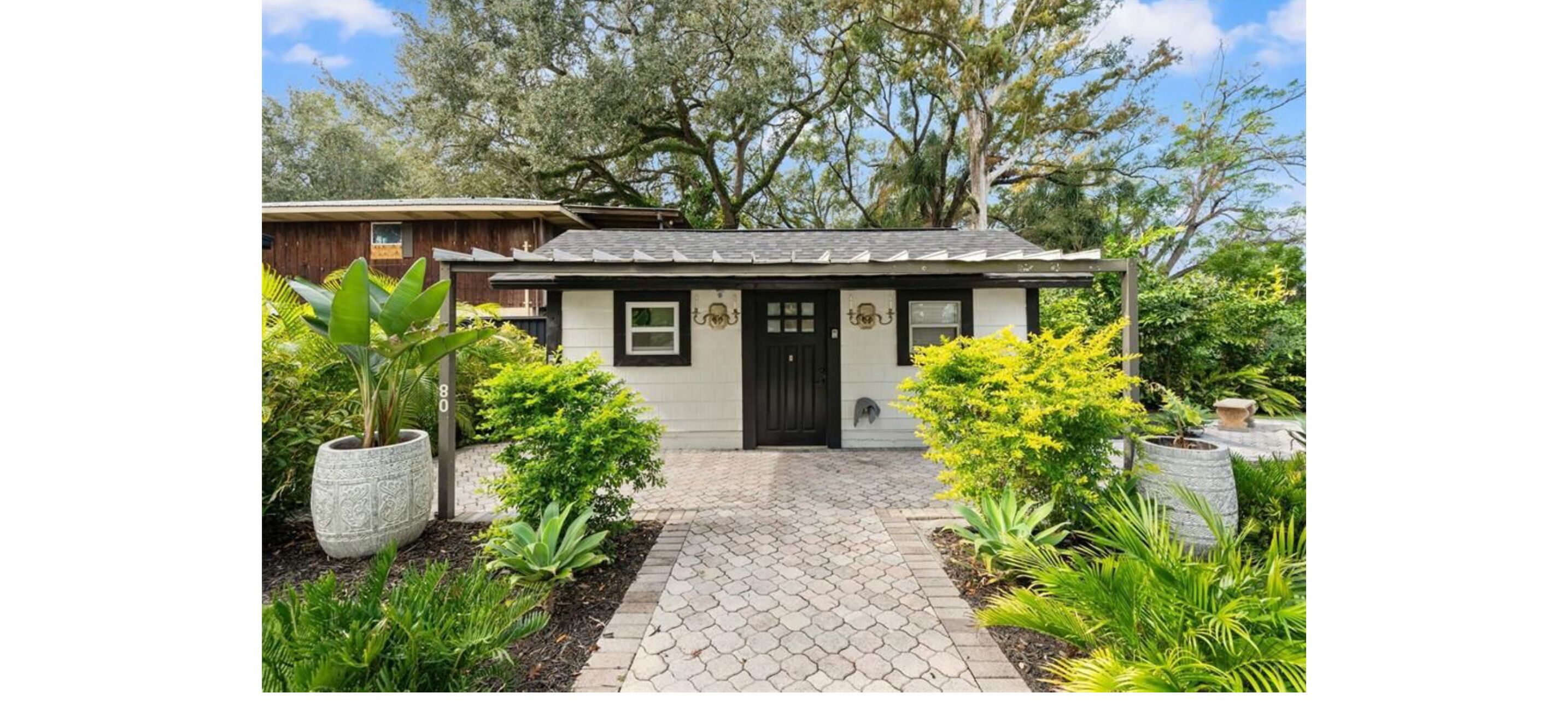 A house with a tiled entrance, surrounded by various plants and trees.
