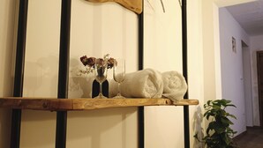 Uno scaffale in legno con un asciugamano, un vaso di vetro con fiori secchi e un bicchiere da vino.