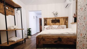 Una camera da letto con un letto di legno, un tappeto verde, uno scaffale in legno con asciugamani e una pianta in vaso.