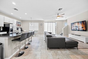 Experience a bright living area with a sleek leather sectional and a large flat-screen TV, ideal for relaxing evenings. The open layout seamlessly connects to a stylish kitchen with modern bar stools, perfect for gatherings. - 4BR house with game room near Disney (Kissimmee)