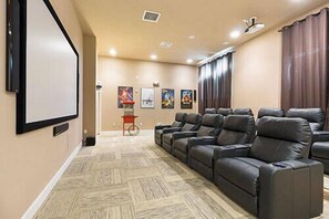 A home theater room with a large screen, multiple reclining seats, and wall-mounted artwork. - 4BR house sleeps 11 with private pool (Kissimmee)