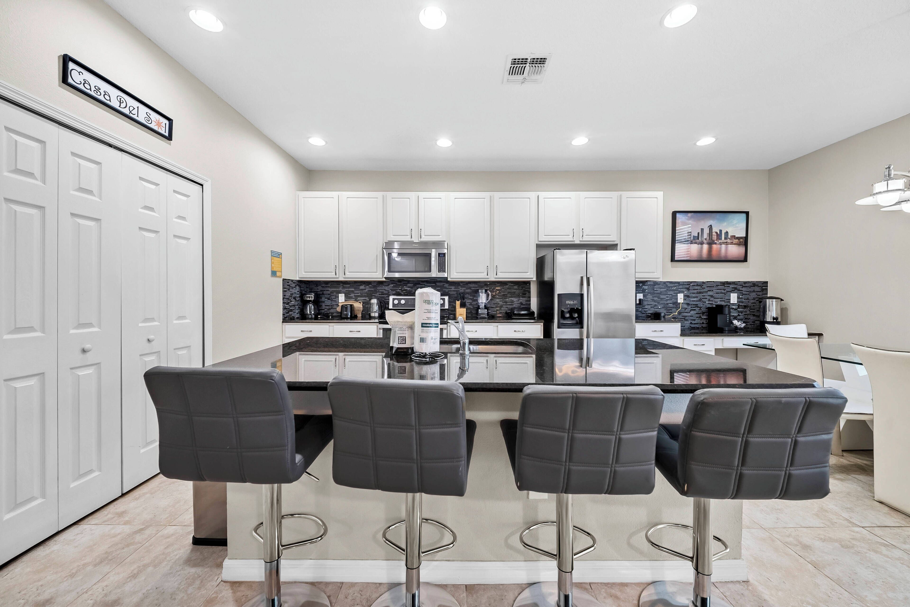 Enjoy a sleek kitchen with a spacious island and stylish bar stools, ideal for casual meals or morning coffee. Glossy cabinets and modern appliances enhance the inviting atmosphere, all under bright overhead lighting.