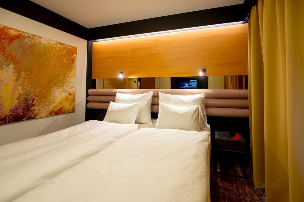 Habitación de hotel con una cama grande, cabecera de madera, televisión montada en la pared y un cuadro.