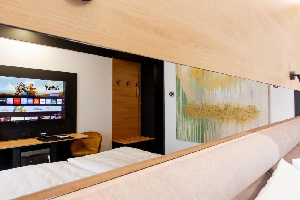 Habitación de hotel moderna con cama, televisor mostrando un juego, escritorio de madera y pared con arte abstracto.