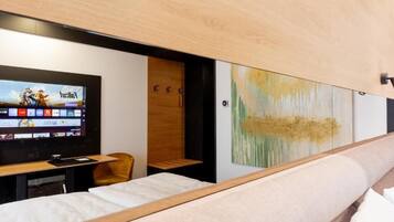 Habitación de hotel moderna con cama, televisor mostrando un juego, escritorio de madera y pared con arte abstracto.