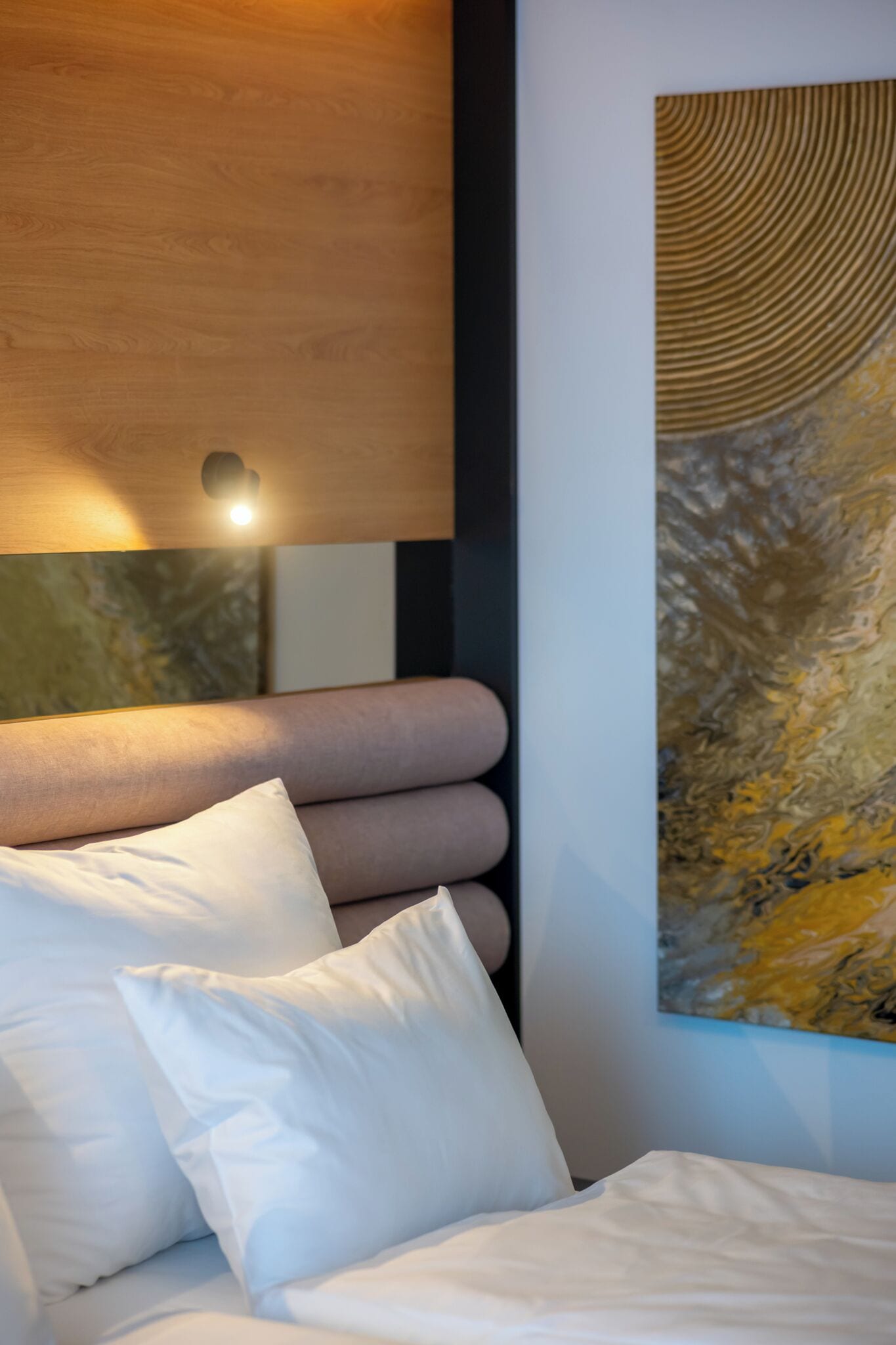 Een bed met witte beddengoed en kussens, een houten hoofdbord en een groot abstract schilderij aan de muur.