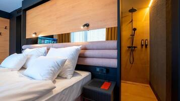 A modern hotel room with a bed, a built-in TV, a shower, and a small bedside table.