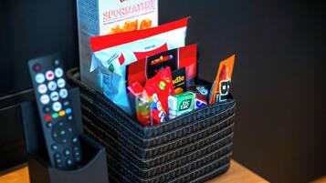 A basket containing snacks and a remote control on a wooden surface.