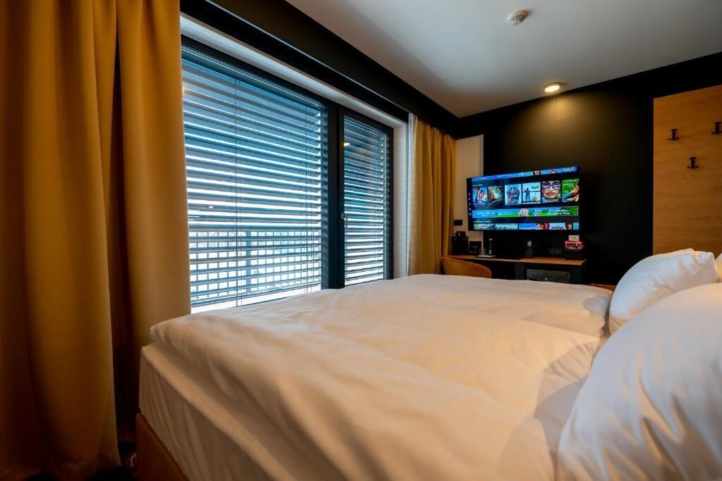 Une chambre d’hôtel avec un grand lit, un téléviseur posé sur un meuble et une fenêtre équipée de stores.