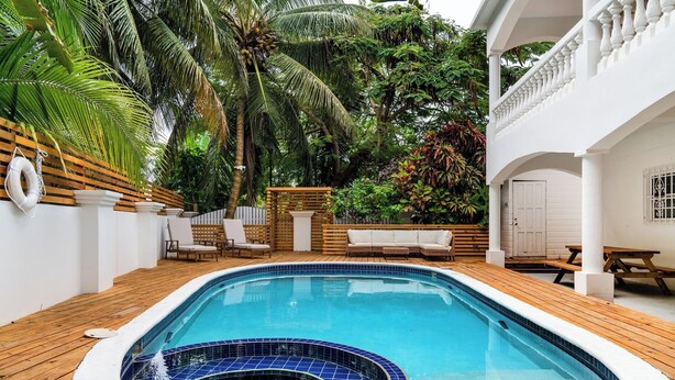 A swimming pool with a hot tub, surrounded by wooden decking and white walls.