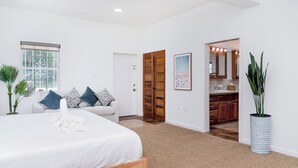 A bedroom with a bed, a sofa, a door, a bathroom, and a potted plant.