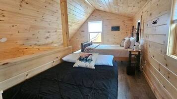 Een slaapkamer in een houten hut met een vide en een kleiner bed, een raam en een nachtkastje.