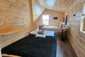 Camera da letto in una baita di legno con letto a soppalco e un letto più piccolo, una finestra e un comodino.