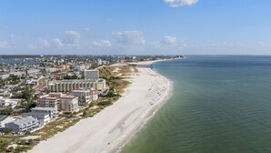 Vista aérea de una ciudad costera con una playa extensa de arena, un puerto deportivo y un complejo hotelero con varias edificaciones.