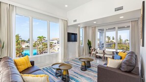 Amplia sala de estar con ventanas grandes, balcón y vista a la piscina.