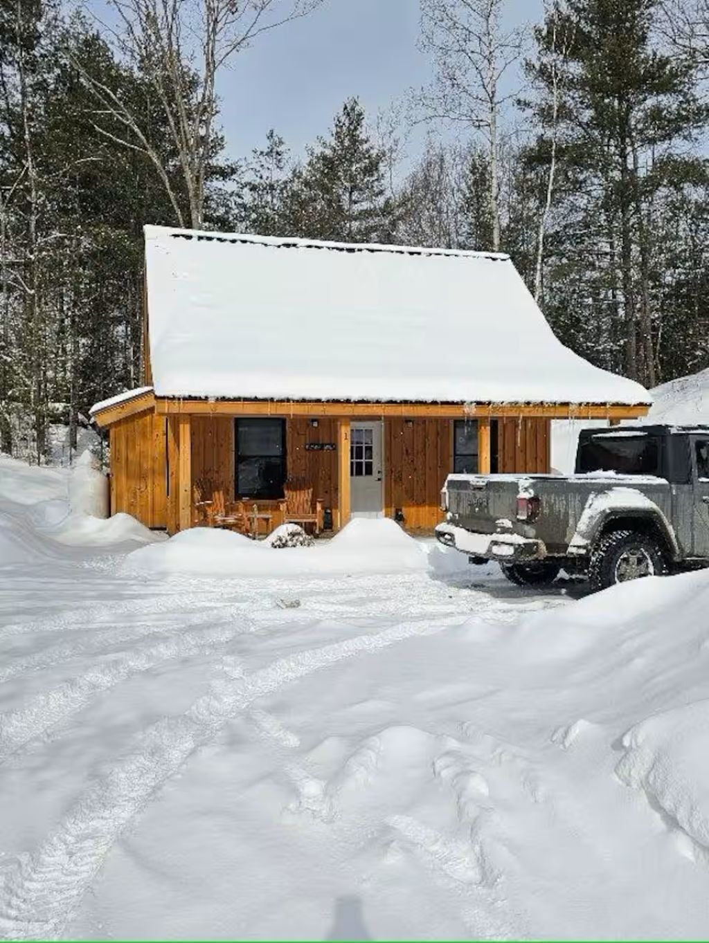 A wooden cabin with a snow-covered roof, a front door, and a vehicle parked in front.