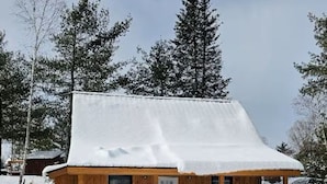 Lumihunnun peittämä puinen mökki, jonka ympärillä on lunta ja puita.