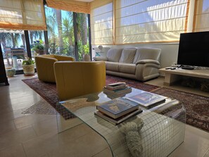 Ein Wohnzimmer mit einer Couch, Sesseln, einem Couchtisch mit Büchern und einem Fernseher.