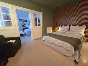 Ein Schlafzimmer mit einem großen Bett, einem Sessel und Blick durch eine offene Tür.