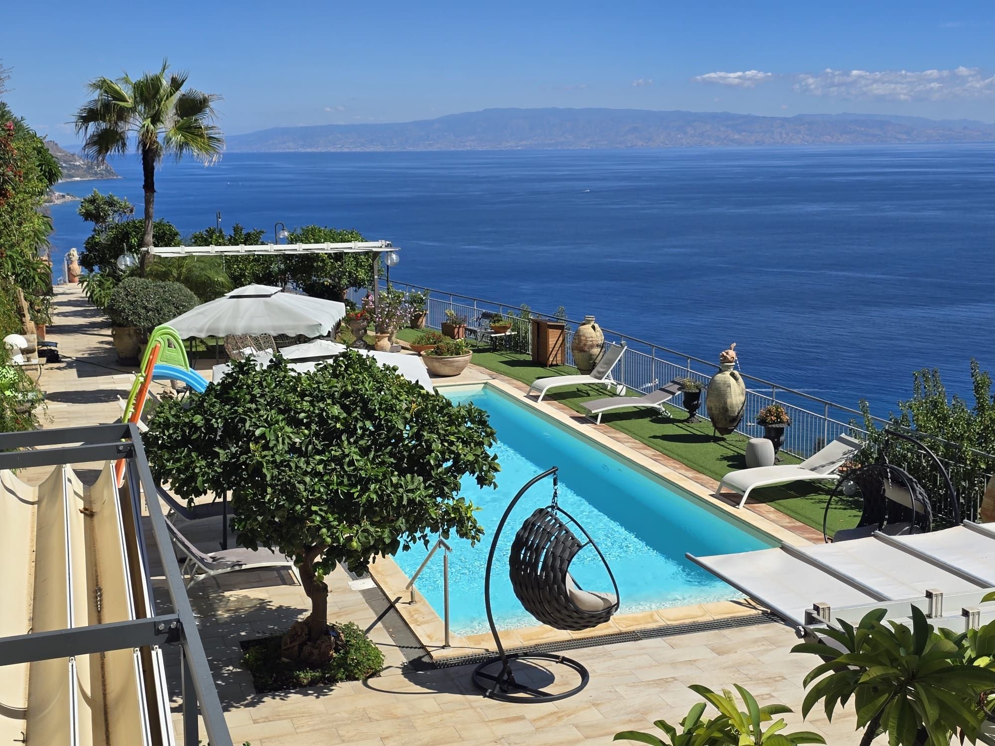 Ein Poolbereich mit einer Hängematte, Liegestühlen und Blick auf das Meer.